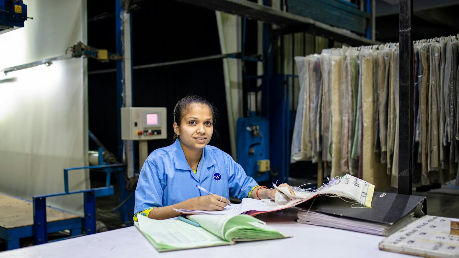 A worker noting fabric details at a workbench beside stacked material samples