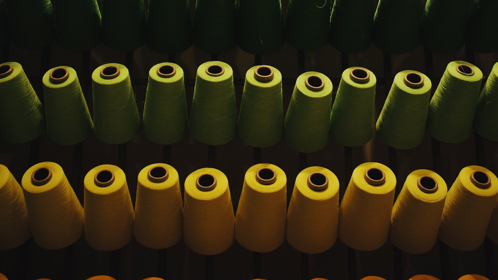 Rows of yarn cones in green and ochre stacked on a mill rack