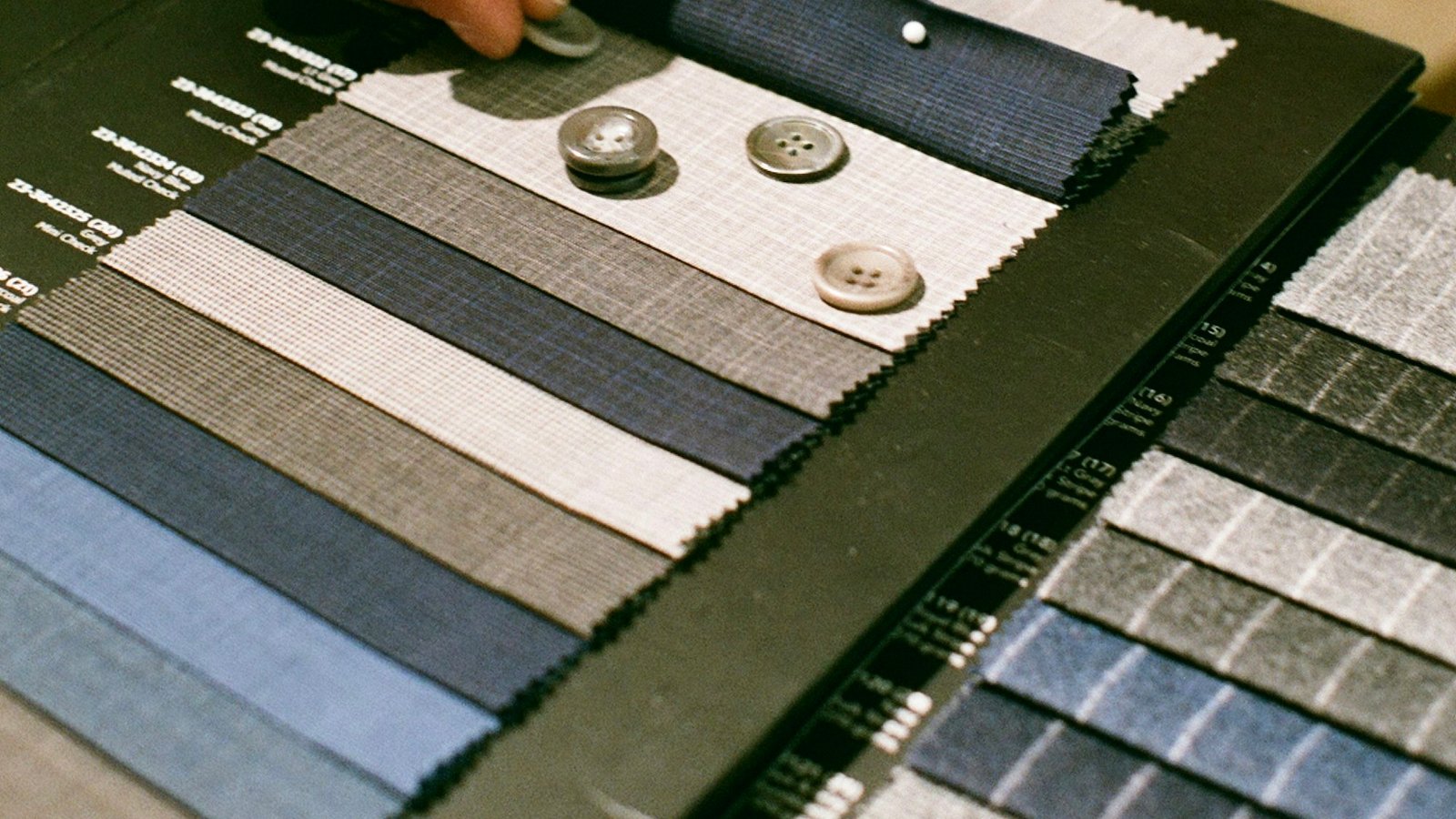 Hands resting on an open book of fabric swatches, with buttons laid alongside