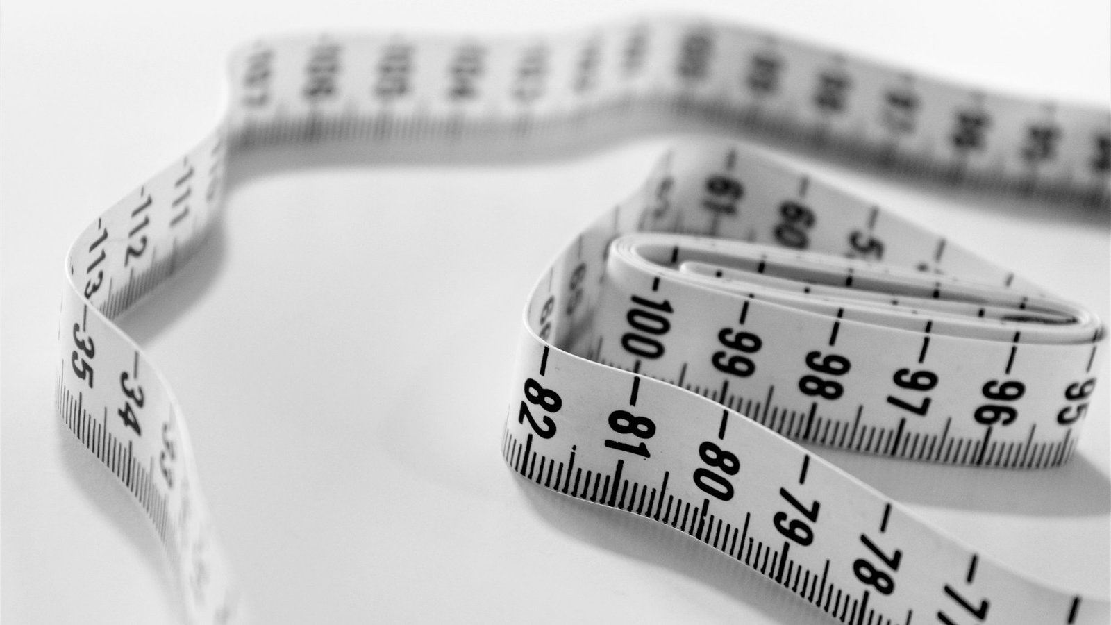 Tailor's measuring tape curled on a white surface, showing centimetre markings
